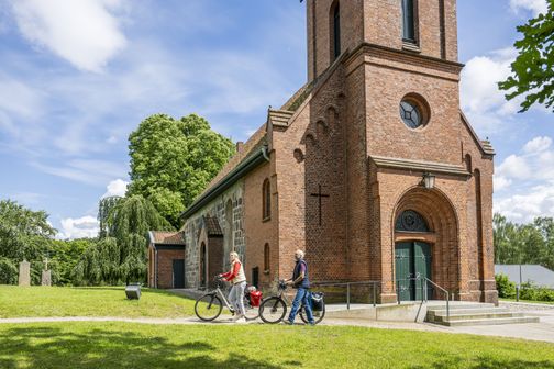 Radreisende gehen entlang der Maria-Magdalenen-Kirche in Malente