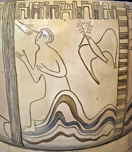 Keramikrelief zeigt eine Figur, die zu einer Hand aufblickt, und einen Vogel mit einem Zweig. Das Design ist schlicht und symbolisch gehalten.