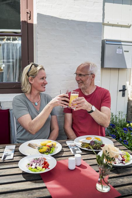 Paar sitzt mit warmen Gerichten vor einem Lokal und stößt an