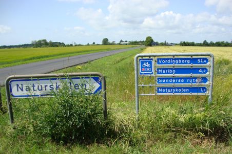 Ein Wegweiser auf einem Radweg in Dänemark zeigt Entfernungen zu verschiedenen Orten.