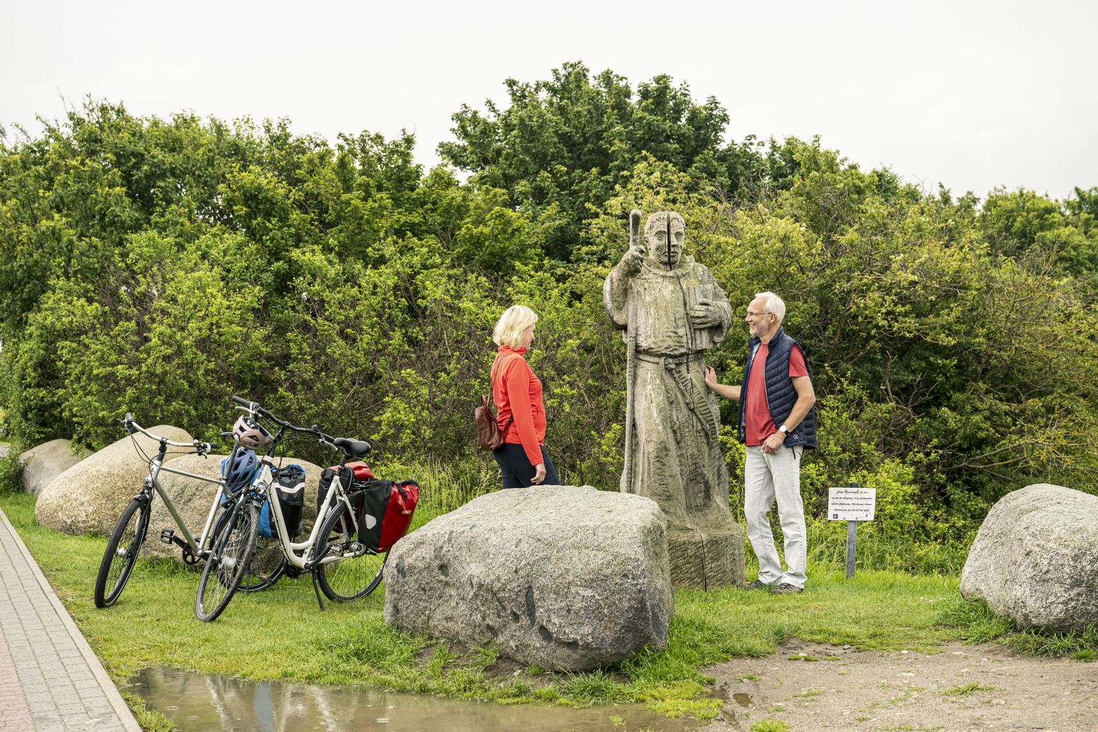 Radreisende betrachten eine Mönchsstatue an der Westmole 