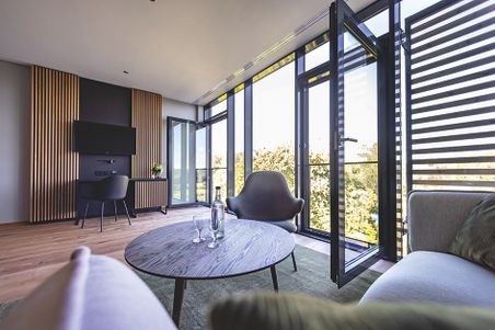 Modernes Hotelzimmer im Hotel Breitenburg mit Panoramafenstern, Sofa, Sessel, Couchtisch und TV-Wand.