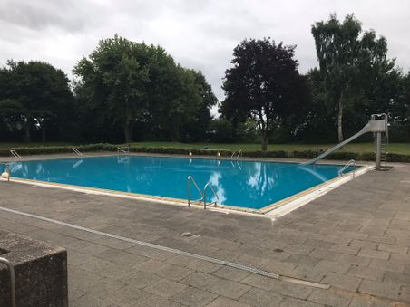 Freibad mit einer Rutsche umgeben von Bäumen.