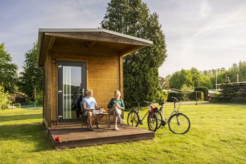 Paar sitzt am Tag vor Tiny-House auf dem Campingsplatz Sonnenkamp