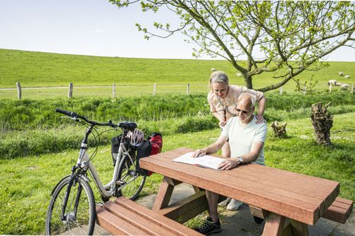 Radreisende machen Pause und studieren eine Karte am Deich