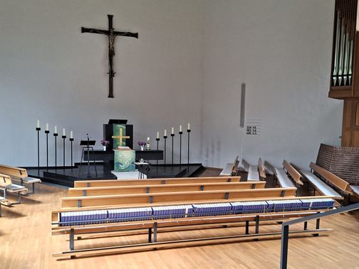 Innenansicht der Friedenskirche Trappenkamp mit Altar, Kreuz und Bänken. Der Raum ist schlicht gestaltet mit Holzboden und Orgel.