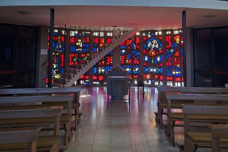 Der Kirchenraum von St. Vicelin in Oldenburg zeigt bunte Glasfenster und Holzbänke. Licht durchflutet den Raum.
