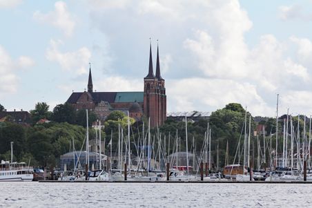 Der Dom zu Roskilde erhebt sich majestätisch über den Hafen, umgeben von Segelbooten und üppigem Grün unter einem bewölkten Himmel.