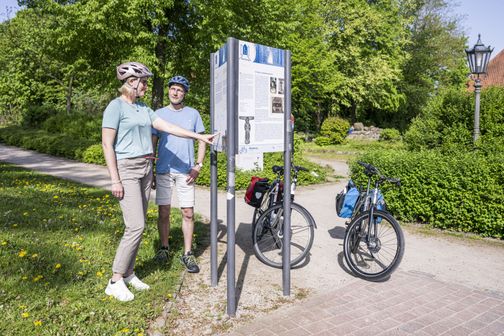 Radreisende schauen sich eine Infotafel an der St. Marien und Bartholomäi Kirche an