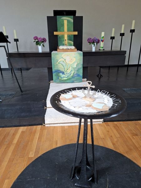 Der Altar der Friedenskirche Trappenkamp ist mit einem Kreuz, Blumen und Kerzen geschmückt. Im Vordergrund steht ein Willkommenstisch mit Sand und Dekoration.