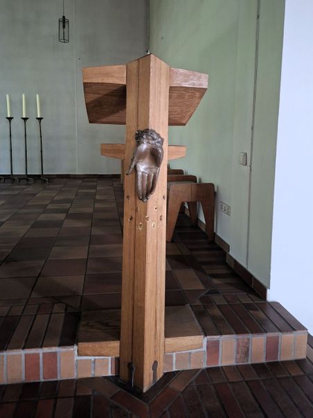 Ein hölzernes Lesepult mit einer bronzenen Hand als Verzierung in einer Kirche. Im Hintergrund stehen drei Kerzenständer.