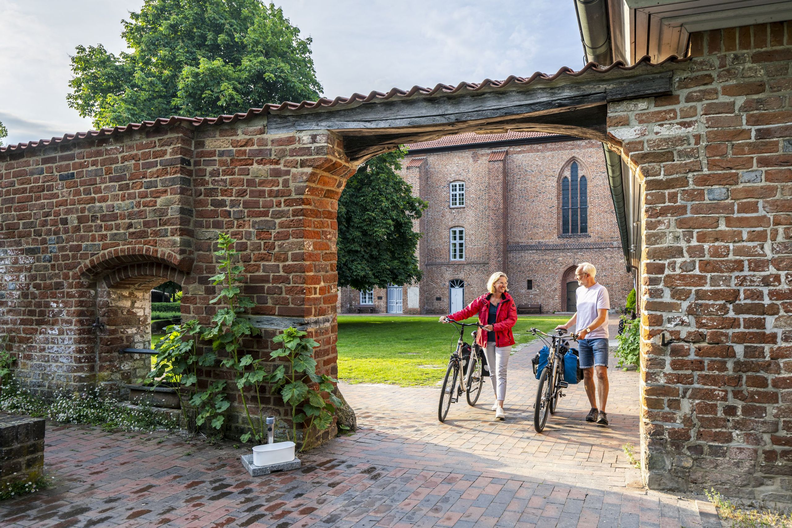 Radreisende gehen über das Gelände des Klosters Cismar