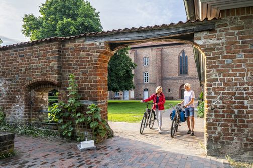 Radreisende gehen über das Gelände des Klosters Cismar
