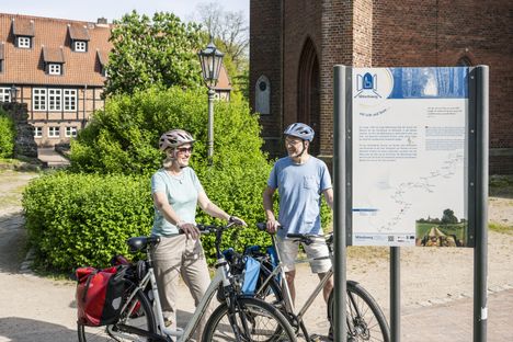 Radreisende stehen vor einer Infotafel an der St. Marien und Bartholomäi Kirche
