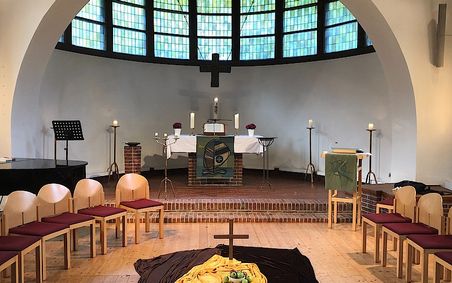 Innenraum einer Kapelle mit Altar, Kerzen, Stühlen und einem Kreuz. 
