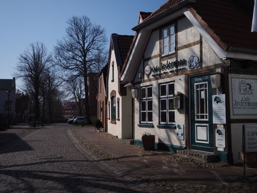 Malerische Altstadtstraße mit Kopfsteinpflaster und dem Café 'Jedermann' an einem sonnigen Tag.